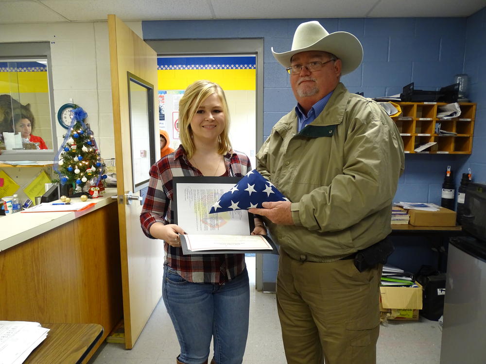 Sheriff Singleton presenting folded flag and paperwork to female high school student